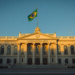 Fachada do prédio da Câmara Municipal de Palhoça com bandeira do Brasil hasteada, representando o novo edital de concurso público